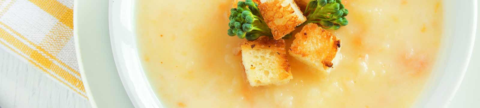 A white bowl of soup with cubed bread garnish